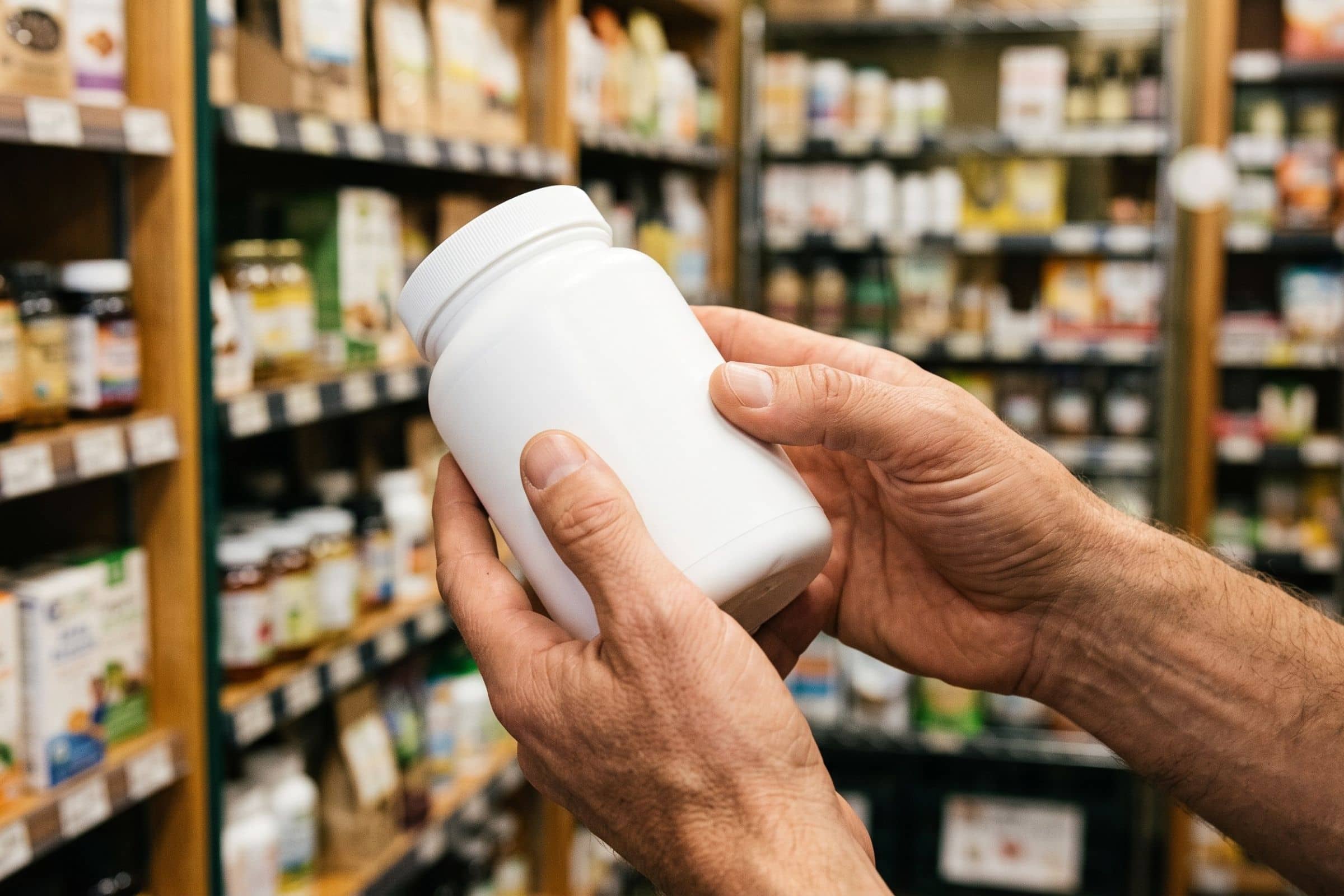 Mains retournant un pot de complément alimentaire pour lire la liste des ingrédients