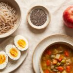 Aliments coupe-faim naturels disposés à plat : konjac, graines de chia, œufs durs, pomme et soupe de légumes