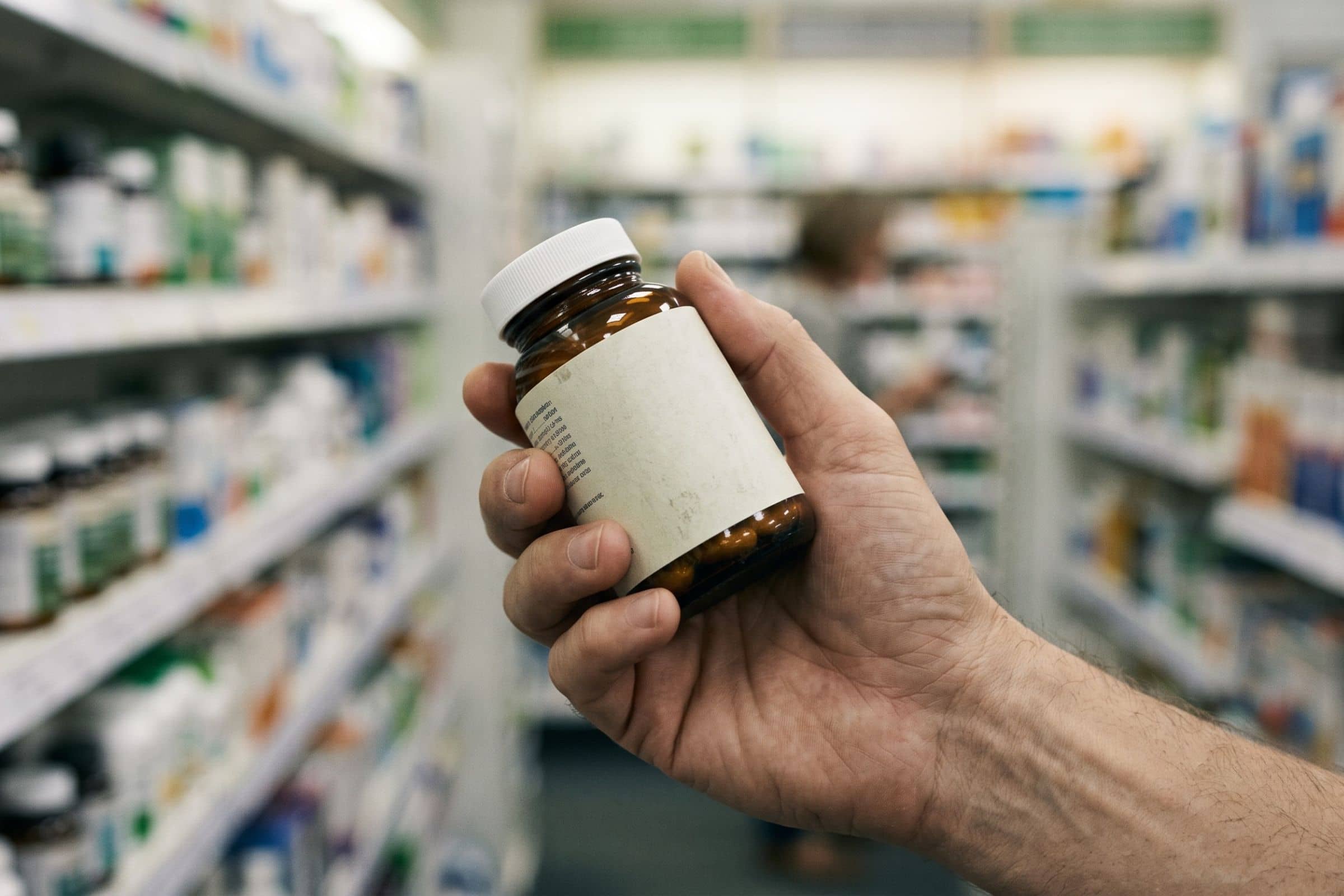 Main tenant un flacon de gélules coupe-faim en rayon parapharmacie, lecture de l'étiquette et du dosage